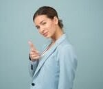 A young woman in a blue suit exhibits confidence with a relaxed pose against a blue background.